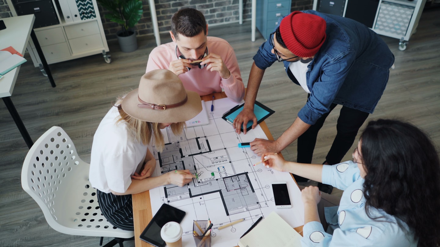 Professionals collaborate on an architectural floor plan at a table.